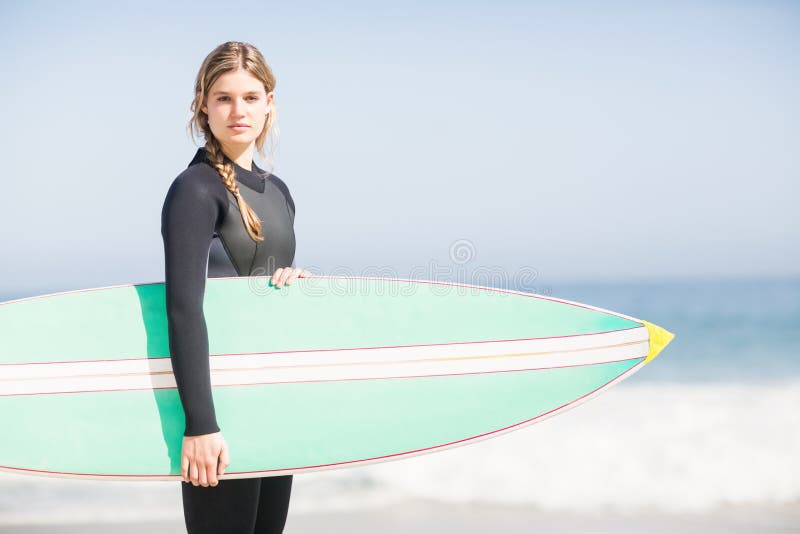 Retrato de la mujer en el wetsuit que sostiene una tabla hawaiana en la playa fotografía de archivo Retrato de la mujer en el wetsuit que sostiene una tabla hawaiana en la playa fotografía de archivo