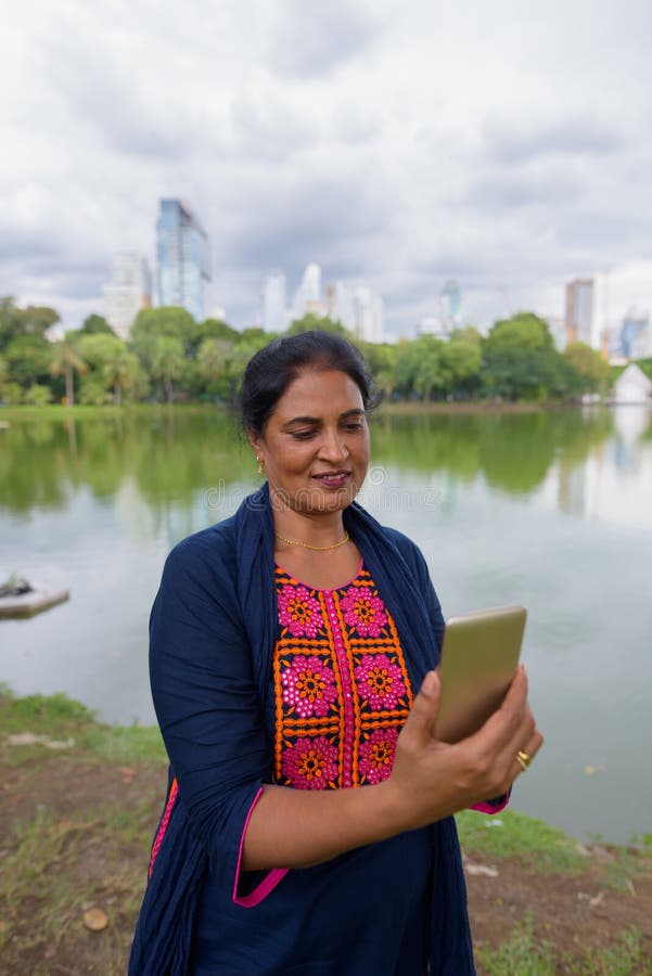 Retrato de la mujer india madura que usa el teléfono móvil en el parque fotografía de archivo libre de regalías Retrato de la mujer india madura que usa el teléfono móvil en el parque fotografía de archivo libre de regalías