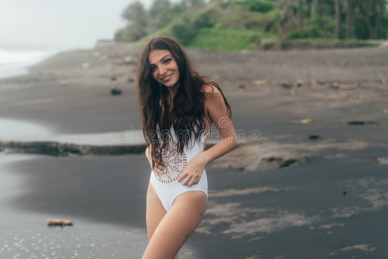 Retrato De La Mujer Joven En El Traje De Baño Blanco Que Presenta En Playa Negra De La Arena Imagen de archivo - Imagen de modelos, bikini: 140492145