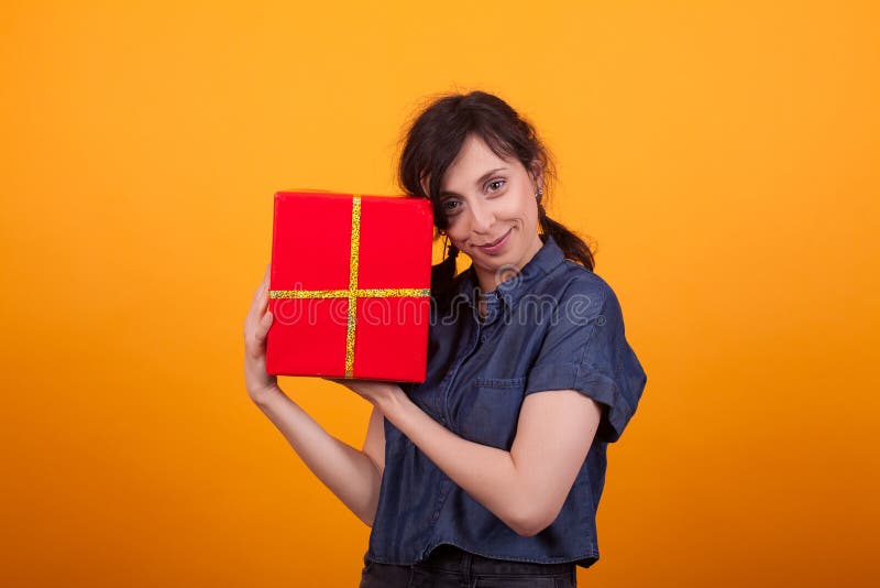 Retrato de la mujer joven feliz con su caja de regalo roja que mira la cámara en estudio sobre fondo amarillo fotografía de archivo Retrato de la mujer joven feliz con su caja de regalo roja que mira la cámara en estudio sobre fondo amarillo fotografía de archivo