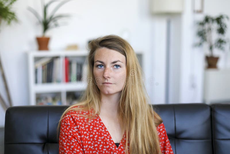 Retrato de la mujer joven seria que se sienta en el sofá imagen de archivo libre de regalías Retrato de la mujer joven seria que se sienta en el sofá imagen de archivo libre de regalías