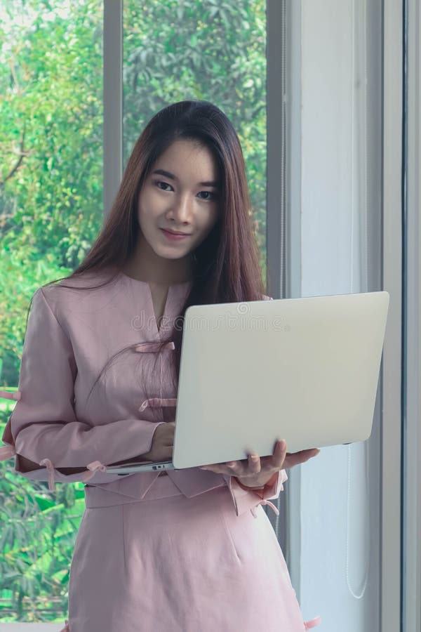 Retrato de la mujer de negocios asiática hermosa y atractiva joven con la sonrisa en labtop rosado del control del vestido en los imágenes de archivo libres de regalías Retrato de la mujer de negocios asiática hermosa y atractiva joven con la sonrisa en labtop rosado del control del vestido en los imágenes de archivo libres de regalías