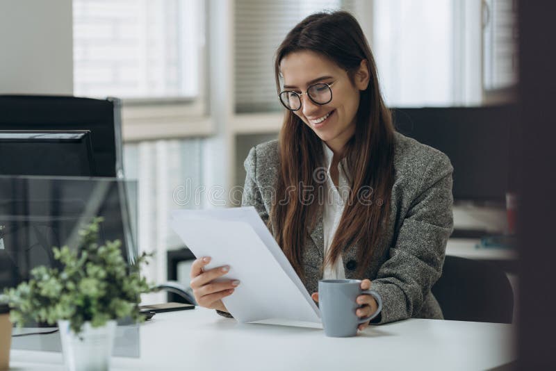 Retrato de la mujer de negocios joven bonita sonriente en los vidrios que se sientan en lugar de trabajo y que trabajan con los d fotografía de archivo Retrato de la mujer de negocios joven bonita sonriente en los vidrios que se sientan en lugar de trabajo y que trabajan con los d fotografía de archivo