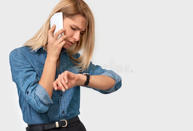 Retrato de la mujer rubia joven frustrada que habla en el teléfono móvil, mirando el reloj, porque su colega es atrasado foto de archivo libre de regalías Retrato de la mujer rubia joven frustrada que habla en el teléfono móvil, mirando el reloj, porque su colega es atrasado foto de archivo libre de regalías