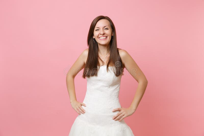 Retrato de la mujer sonriente alegre de la novia en la situación blanca hermosa del vestido del cordón que se casa con en jarras