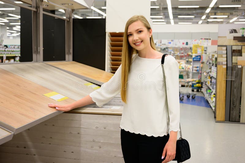 Retrato de la mujer sonriente joven que elige el suelo laminado de madera en tienda foto de archivo libre de regalías Retrato de la mujer sonriente joven que elige el suelo laminado de madera en tienda foto de archivo libre de regalías
