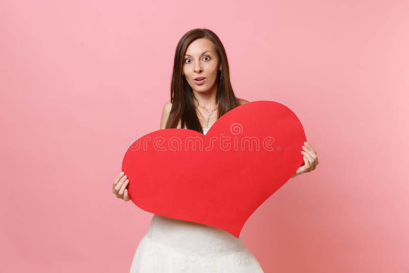 Retrato de la mujer sorprendente chocada de la novia en el vestido que se casa blanco hermoso que lleva a cabo el corazón rojo en imagenes de archivo Retrato de la mujer sorprendente chocada de la novia en el vestido que se casa blanco hermoso que lleva a cabo el corazón rojo en imagenes de archivo