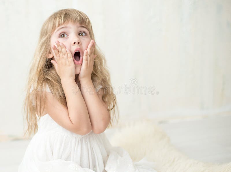 Portrait of pretty little girl in white dress , she is surprised and put her hands on cheeks. She is happy and waiting for a moment. Portrait of pretty little girl in white dress , she is surprised and put her hands on cheeks. She is happy and waiting for a moment.