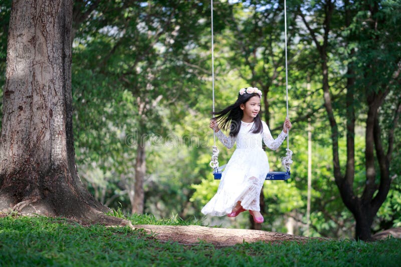 Retrato de la pequeña muchacha asiática que juega el oscilación debajo del árbol grande con la profundidad baja del foco selecto foto de archivo libre de regalías Retrato de la pequeña muchacha asiática que juega el oscilación debajo del árbol grande con la profundidad baja del foco selecto foto de archivo libre de regalías