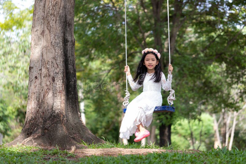 Retrato de la pequeña muchacha asiática que juega el oscilación debajo del árbol grande en el bosque de la naturaleza con tono su fotografía de archivo libre de regalías Retrato de la pequeña muchacha asiática que juega el oscilación debajo del árbol grande en el bosque de la naturaleza con tono su fotografía de archivo libre de regalías