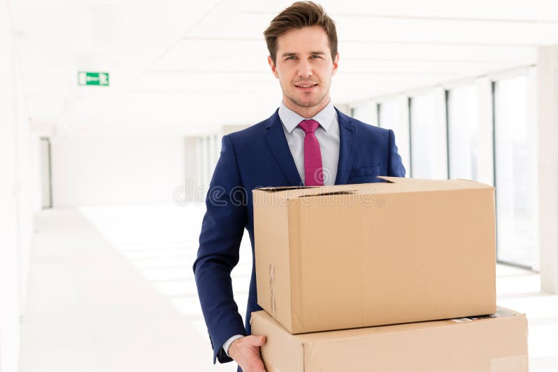 Retrato de las cajas de cartón del hombre de negocios que llevan joven en nueva oficina imágenes de archivo libres de regalías Retrato de las cajas de cartón del hombre de negocios que llevan joven en nueva oficina imágenes de archivo libres de regalías
