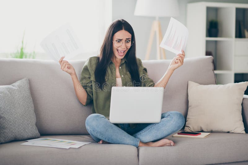 Retrato de loca desesperada abrumada chica sentada en el diván usando laptop analizando documentos fail informe en casa imágenes de archivo libres de regalías