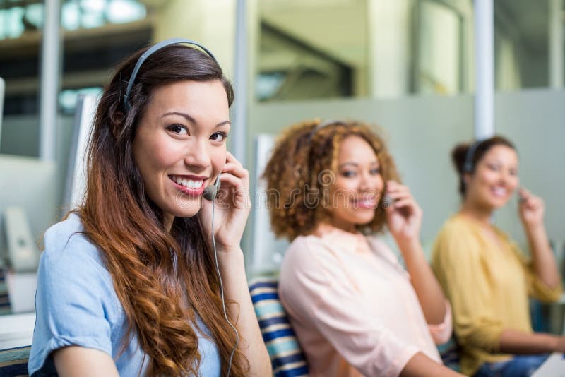 Retrato de los ejecutivos de sexo femenino del servicio de atención al cliente que hablan en las auriculares en el escritorio foto de archivo Retrato de los ejecutivos de sexo femenino del servicio de atención al cliente que hablan en las auriculares en el escritorio foto de archivo