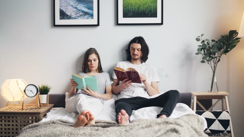 Retrato de los libros de lectura de la muchacha y del individuo en cama en casa en el apartamento ligero