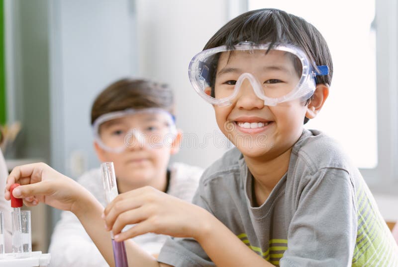 Portrait of little scientist Asian boy in safety glasses smiling at the camera while examining a test tube in science class. Elementary School Science Classroom. Children Learn with Interest. Portrait of little scientist Asian boy in safety glasses smiling at the camera while examining a test tube in science class. Elementary School Science Classroom. Children Learn with Interest