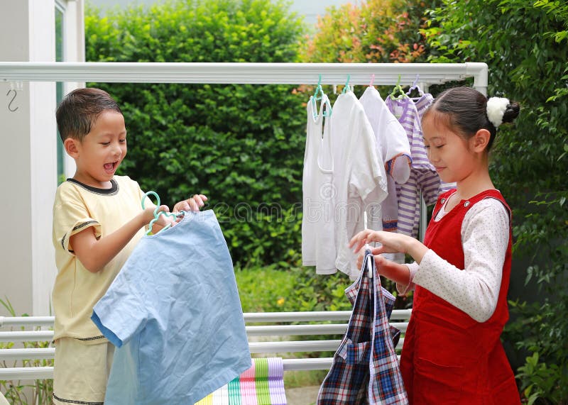Retrato de muchacha y niño asiáticos ayudando a secar la ropa en el jardín cerca de la casa. Hermana y hermanito ayudan a las tare imágenes de archivo libres de regalías