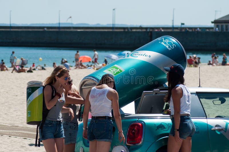 Retrato de muchachas atractivas con los vaqueros cortos y la camiseta blanca que da las latas rojas frescas del toro en la playa imagen de archivo Retrato de muchachas atractivas con los vaqueros cortos y la camiseta blanca que da las latas rojas frescas del toro en la playa imagen de archivo