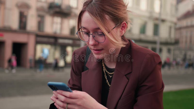 Retrato de mujer caucásica feliz con gafas escribiendo por teléfono móvil al aire libre. cerrando a una alegre chica caminando con