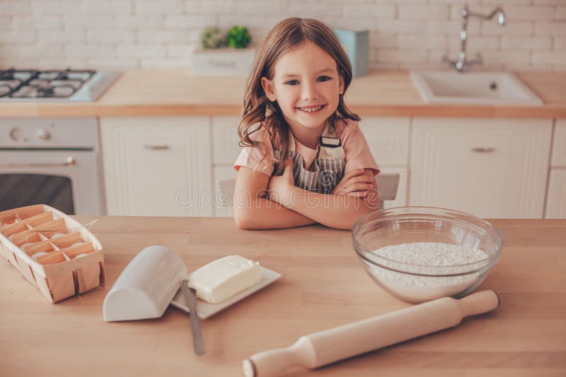 Retrato de niña de pie en la mesa de la cocina con las manos cruzadas mirando a la cámara imagen de archivo