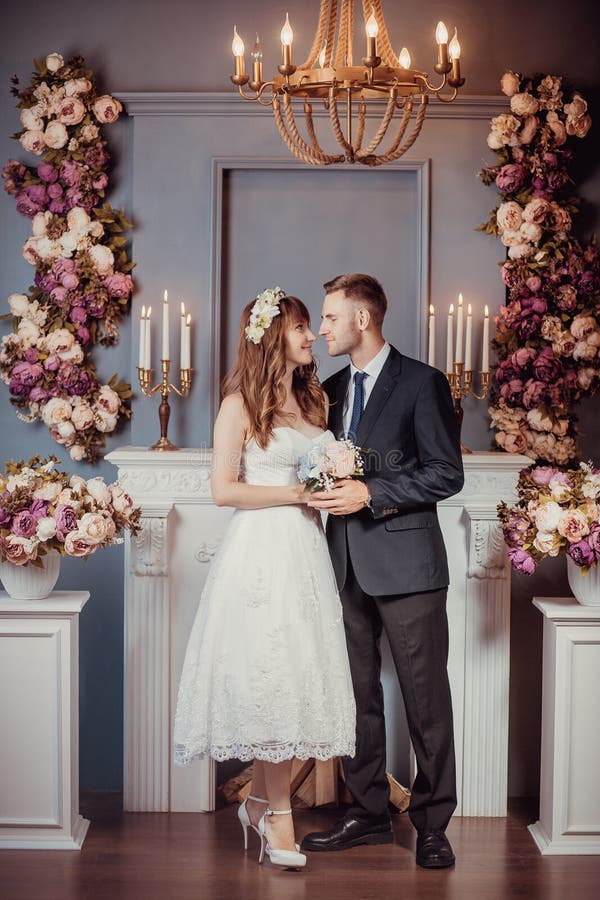 Retrato de noivos novos felizes em um interior clássico perto da chaminé com flores Dia do casamento, tema do amor Primeiro dia imagem de stock Retrato de noivos novos felizes em um interior clássico perto da chaminé com flores Dia do casamento, tema do amor Primeiro dia imagem de stock