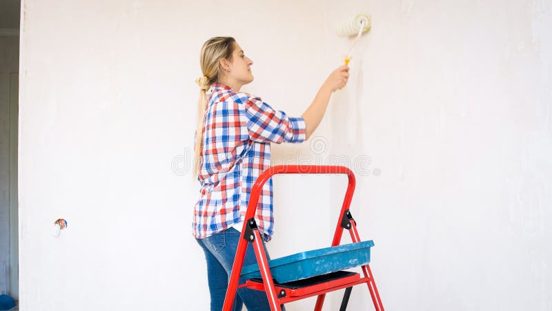 Retrato de paredes bonitas da pintura da jovem mulher em sua casa nova imagem de stock Retrato de paredes bonitas da pintura da jovem mulher em sua casa nova imagem de stock