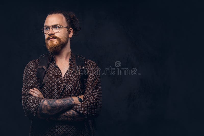 Retrato de um estudante do moderno do ruivo nos vidros vestidos em uma camisa marrom, posses uma trouxa, levantando em um estúdio imagem de stock Retrato de um estudante do moderno do ruivo nos vidros vestidos em uma camisa marrom, posses uma trouxa, levantando em um estúdio imagem de stock