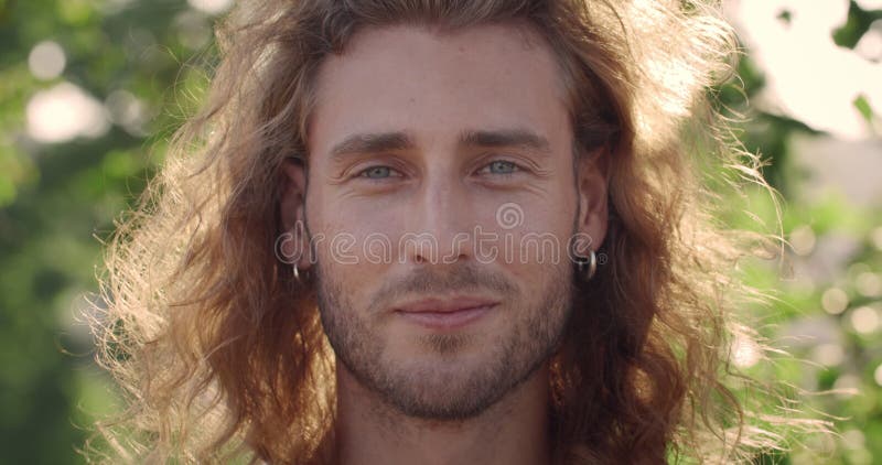 Vista de perfil de um homem bonito com cabelo loiro olhando para a câmera  ao ar livre