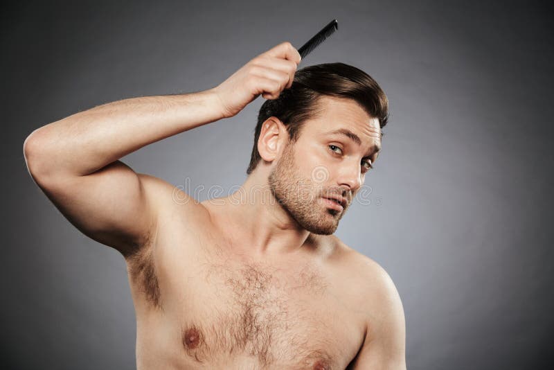 Retrato de um homem descamisado concentrado que penteia seu cabelo foto de stock Retrato de um homem descamisado concentrado que penteia seu cabelo foto de stock