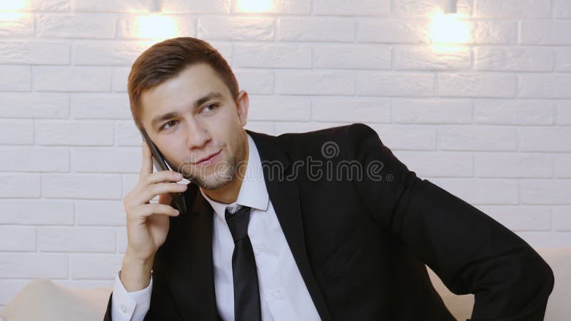 Retrato de um homem novo em um terno preto que fala no telefone