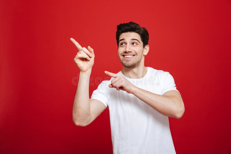 Retrato de um homem novo de sorriso em apontar branco do t-shirt fotos de stock Retrato de um homem novo de sorriso em apontar branco do t-shirt fotos de stock