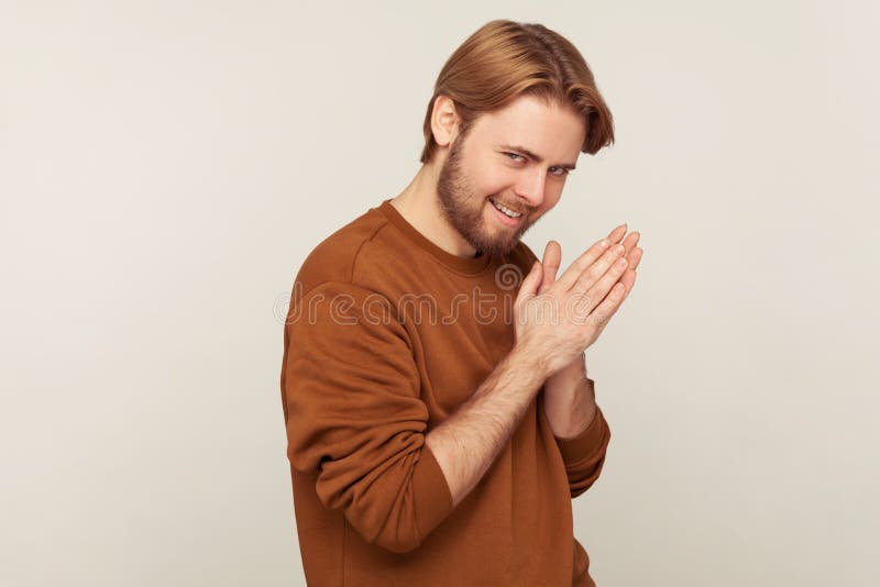 Retrato de um homem sorrateiro com barba vestida de camisola esfregando palma como tendo uma ideia maléfica astuta