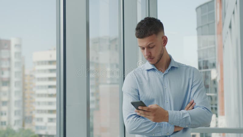 Retrato de um jovem empresário no escritório que fica parado à janela com um olhar penoso pensando em estratégia empresarial e