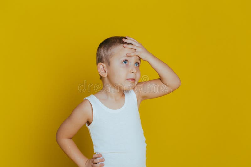 Retrato de um rapaz pequeno pensativo atrativo com em uma veste branca que guarda uma m?o em sua cabe?a imagem de stock Retrato de um rapaz pequeno pensativo atrativo com em uma veste branca que guarda uma m?o em sua cabe?a imagem de stock
