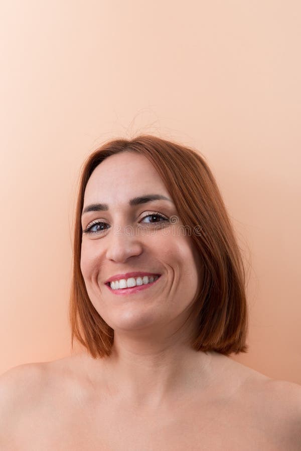 Portrait of a beautiful 30 years old Caucasian woman with short red hair and wide smile looking at camera on peach color background. Copy space. Natural beauty concept. Portrait of a beautiful 30 years old Caucasian woman with short red hair and wide smile looking at camera on peach color background. Copy space. Natural beauty concept