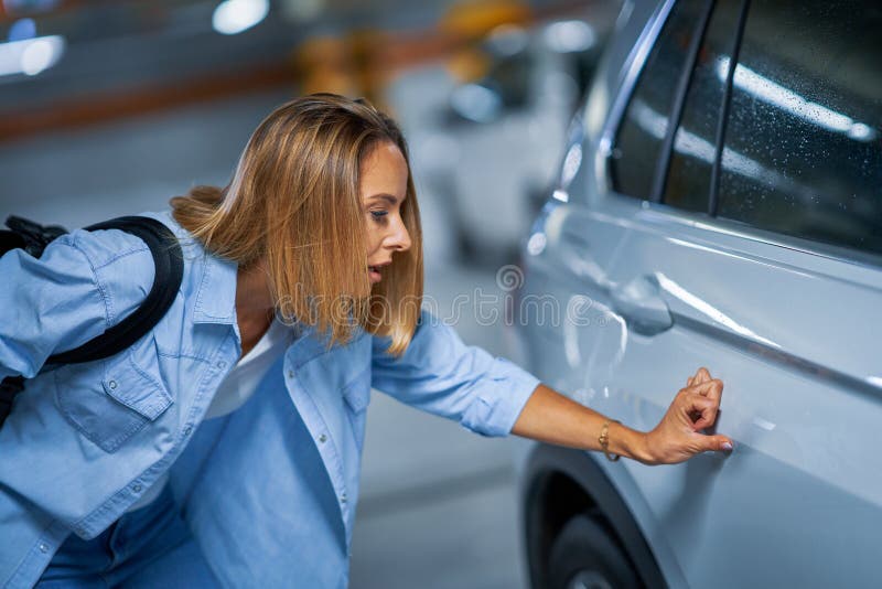 Retrato de uma jovem com carro arranhado no estacionamento subterrâneo