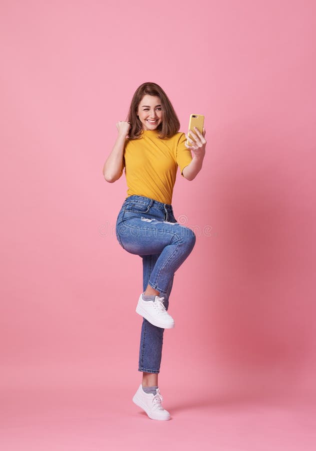 Retrato de uma jovem feliz celebrando com o telefone celular sobre fundo rosa imagem de stock Retrato de uma jovem feliz celebrando com o telefone celular sobre fundo rosa imagem de stock