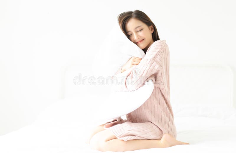 Retrato de uma menina asiática de sorriso nova no rosa da camiseta que abraça um descanso que senta-se em uma cama em seu quarto foto de stock royalty free Retrato de uma menina asiática de sorriso nova no rosa da camiseta que abraça um descanso que senta-se em uma cama em seu quarto foto de stock royalty free