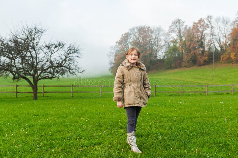 Outdoor portrait of a cute little girl in a garden on a foggy day, wearing warm beige coat. Outdoor portrait of a cute little girl in a garden on a foggy day, wearing warm beige coat