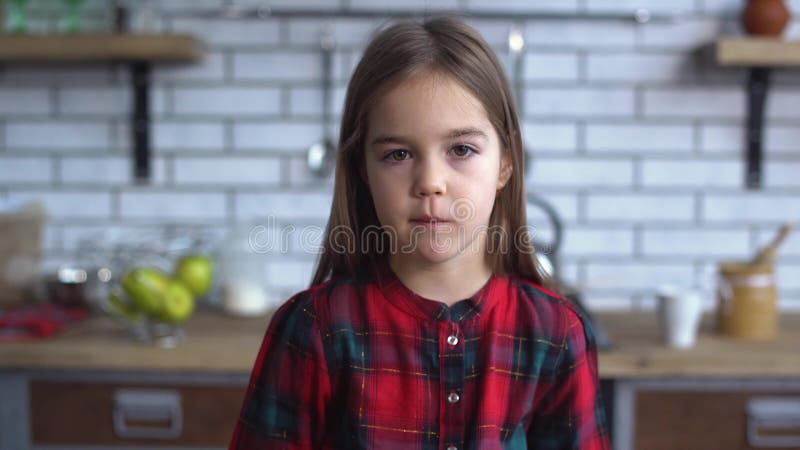 Retrato de uma menina de sorriso pequena bonito em uma posição quadriculado da camisa na cozinha