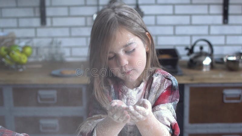 Retrato de uma menina sujada pesadamente na farinha de sopro da farinha de sua palma Menina bonito que tem o divertimento na cozi