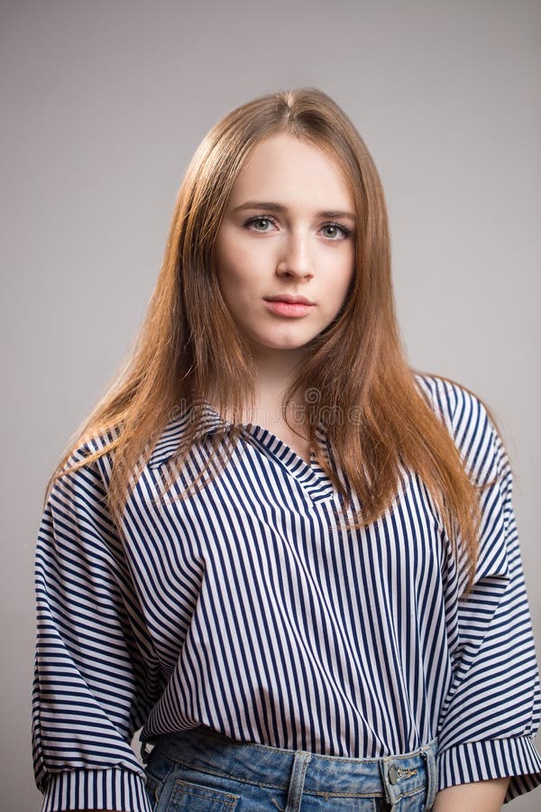 Retrato de uma mulher bonita do ruivo que veste uma blusa listrada e que olha a câmera em um fundo cinzento Menina nova do estuda fotos de stock royalty free Retrato de uma mulher bonita do ruivo que veste uma blusa listrada e que olha a câmera em um fundo cinzento Menina nova do estuda fotos de stock royalty free
