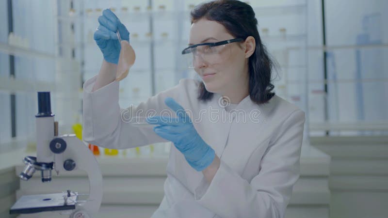 Retrato de uma mulher cientista em um casaco branco com pinças nas mãos olhando para a carne artificialmente cultivada de uma petr