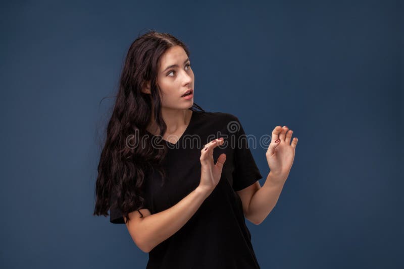 Retrato de uma mulher moreno de cabelos compridos no t-shirt preto que levanta em um fundo cinzento e que mostra emoções difere imagem de stock Retrato de uma mulher moreno de cabelos compridos no t-shirt preto que levanta em um fundo cinzento e que mostra emoções difere imagem de stock
