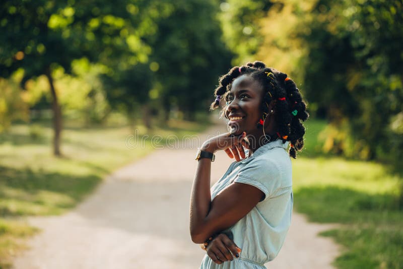 Retrato de uma mulher negra nova de sorriso da beleza africana em um parque com alargamento da luz solar e espaço da cópia fotografia de stock royalty free Retrato de uma mulher negra nova de sorriso da beleza africana em um parque com alargamento da luz solar e espaço da cópia fotografia de stock royalty free