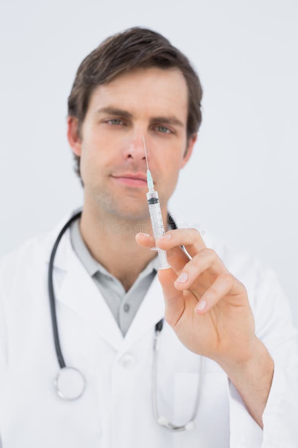 Retrato de un doctor de sexo masculino hermoso que celebra una inyección imagenes de archivo Retrato de un doctor de sexo masculino hermoso que celebra una inyección imagenes de archivo