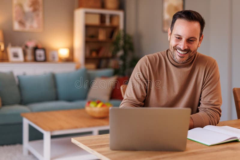 Retrato de un empresario apuesto que revisa los correos electrónicos sobre una laptop mientras está sentado en su oficina en casa foto de archivo libre de regalías
