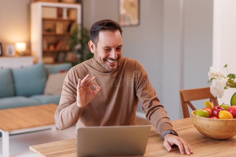 Retrato de un feliz trabajador independiente que muestra el signo correcto mientras habla sobre una videollamada en una laptop en imagen de archivo