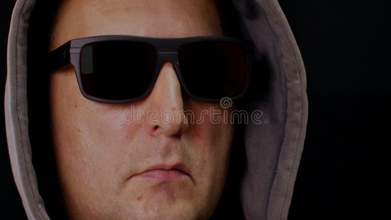 Retrato de un hombre adulto con gafas negras y capucha sobre fondo oscuro. cara masculina en gafas de sol y cabeza de cabeceo del