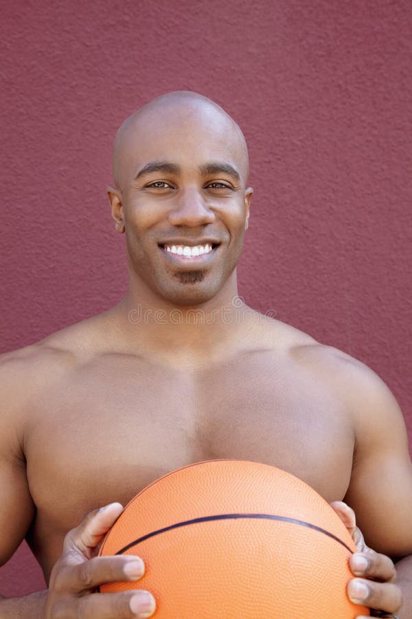 Retrato de un hombre afroamericano descamisado con baloncesto sobre fondo coloreado foto de archivo
