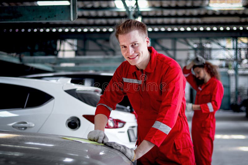 Retrato de un hombre mecánico sonriente con uniforme rojo parado alrededor de los coches de los vehículos en el taller de revisión foto de archivo